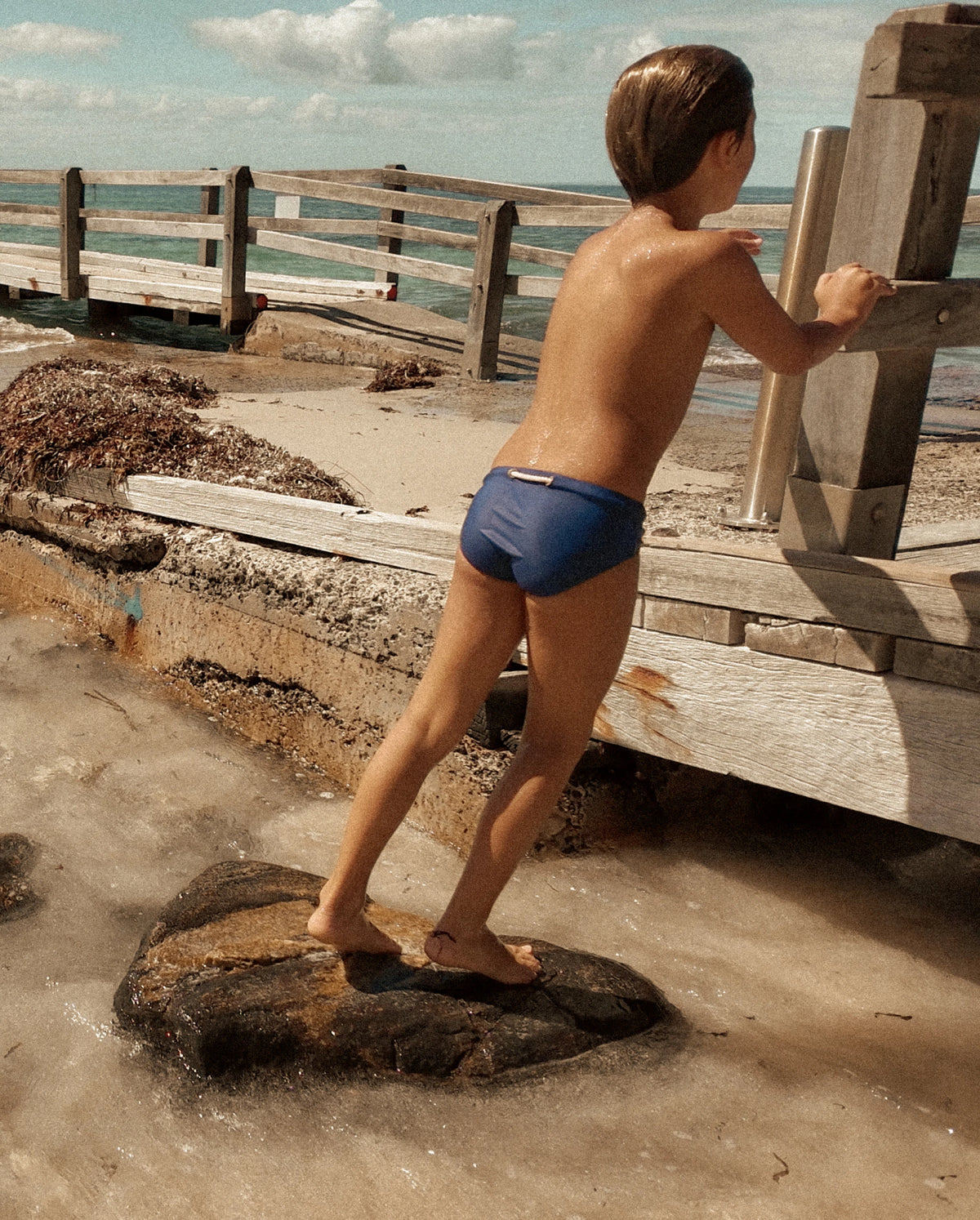 Child wearing navy Lobby’s Nippers by the ocean, featuring the signature rope detail at the back waistband.