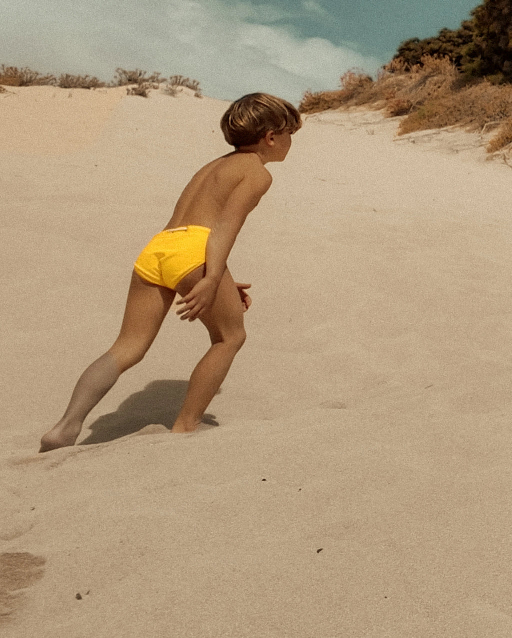 Child wearing yellow Lobby’s Nippers running across the sand, showcasing the swim briefs in motion.
