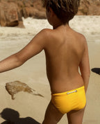 Back view of a child wearing yellow Lobby’s Nippers on the beach, featuring the signature rope waistband detail.
